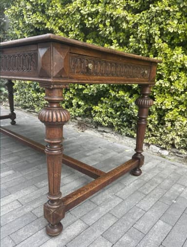 A long, narrow dark wood table, featuring a rectangular top and heavily carved apron and turned legs. The legs are connected by a rectangular stretcher base, presenting a traditional or antique aesthetic. — 3D model