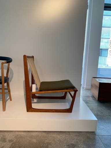 A contemporary armless lounge chair with a low-slung profile, featuring a visible, light-toned wooden frame. The seat and backrest are upholstered in an olive green fabric, presenting a clean and minimalist aesthetic. The chair's design emphasizes simple geometric lines and comfort for relaxation. — 3D model