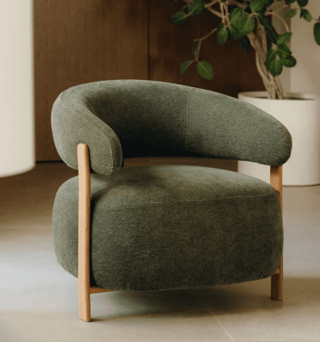A contemporary armchair featuring a rounded, barrel-style design upholstered in a deep olive green fabric, supported by a minimalist exposed light wood frame. — 3D model