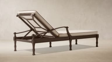 A dark bronze finished metal chaise lounge designed for outdoor use, featuring an adjustable backrest and thick, off-white cushions with dark brown piping. The frame exhibits classic design elements with shaped legs and armrests. — 3D model