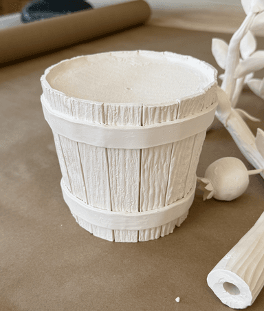 A white, cylindrical planter designed to resemble a wooden barrel. The exterior is constructed from vertical wooden staves, textured to mimic wood grain, and secured by two horizontal bands. The top rim is flat and slightly textured. It appears to be a decorative item for holding plants. — 3D model