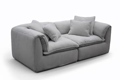 A contemporary deep-seated sofa, upholstered in a light gray textured fabric, featuring plush, loose seat and back cushions for maximum comfort. The design includes additional throw pillows and boasts a clean, monolithic silhouette with fully upholstered arms and base. — 3D model