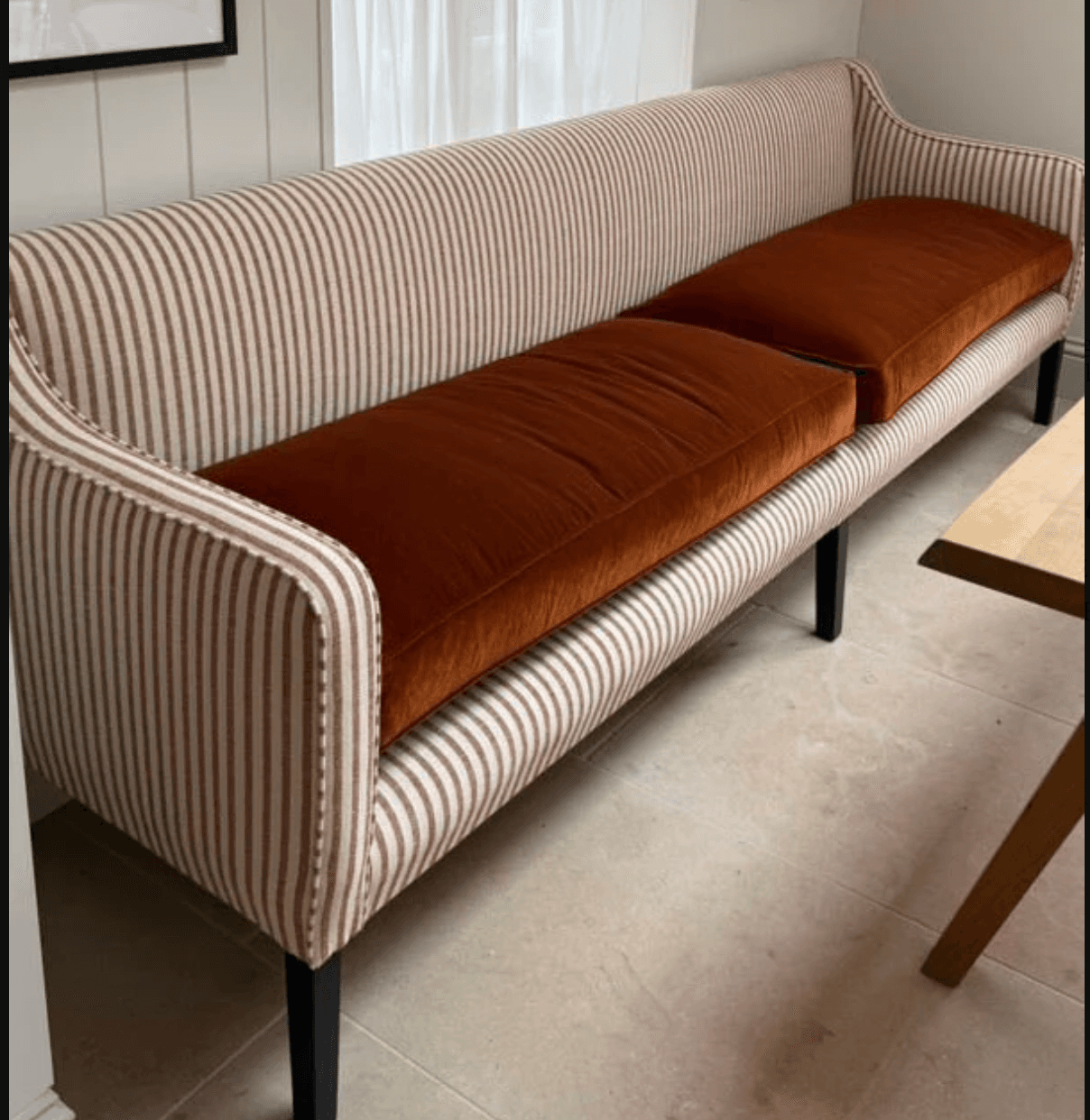 A contemporary banquette-style loveseat with a high, gently curved back and no distinct armrests. It features vertically striped upholstery in beige and brown on the frame, paired with two removable, solid reddish-brown seat cushions. The piece is supported by four slender, tapered dark legs. — 3D model