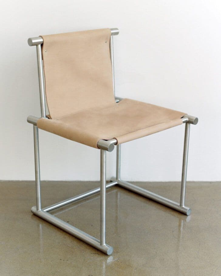 A modern armless chair featuring a tubular metal frame with a natural leather sling seat and back, designed with a minimalist and industrial aesthetic. — 3D model
