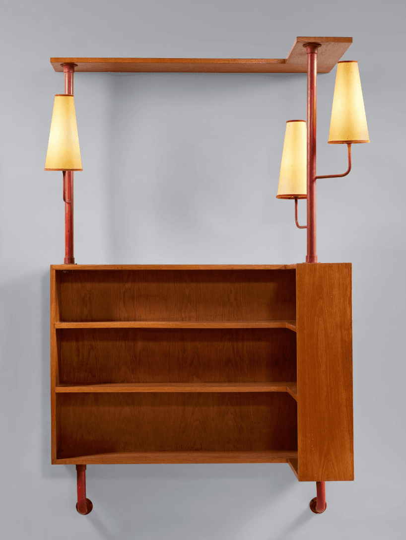 A modular shelving unit constructed with wooden shelves and a red metal frame. The unit features multiple open shelves on the left and a closed cabinet section on the right. Integrated into the upper frame are two lamps with conical, cream-colored shades, attached to red metal arms extending from vertical support posts. — 3D model