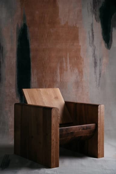 A robust, modern armchair constructed from solid wood, featuring a block-style frame in a dark finish and a distinct, angled backrest in a lighter wood tone. The design emphasizes clean lines and substantial material, giving it a minimalist yet impactful presence. — 3D model