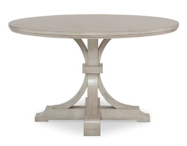 A round pedestal dining table with a light-colored finish. The table features a thick, banded tabletop with a subtle beveled edge. The pedestal base consists of a central square column from which four curved supports fan out, connecting to a wider, rectangular base with decorative moldings. The overall design suggests a transitional or modern farmhouse style. — 3D model