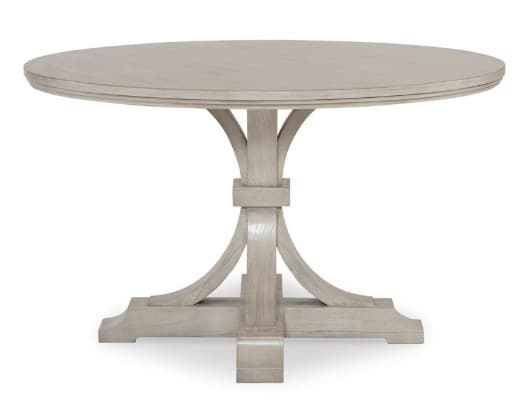 A round pedestal dining table with a light-colored finish. The table features a thick, banded tabletop with a subtle beveled edge. The pedestal base consists of a central square column from which four curved supports fan out, connecting to a wider, rectangular base with decorative moldings. The overall design suggests a transitional or modern farmhouse style. — 3D model