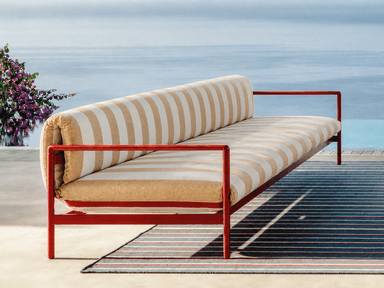 An elongated seating unit featuring a minimalist red metal frame and striped cushions, designed for lounging. It has integrated armrests and a cylindrical back bolster. — 3D model