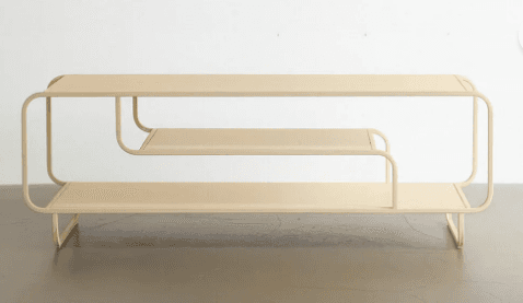 A low, two-tiered shelving unit made from tubular metal with flat shelves, featuring a continuous, bent frame with rounded edges and finished in a light beige color. — 3D model
