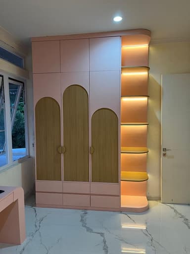 A modern, tall storage unit in pink with natural wood accents, featuring multiple closed cabinet doors, base drawers, and integrated, illuminated corner shelves on one side. — 3D model