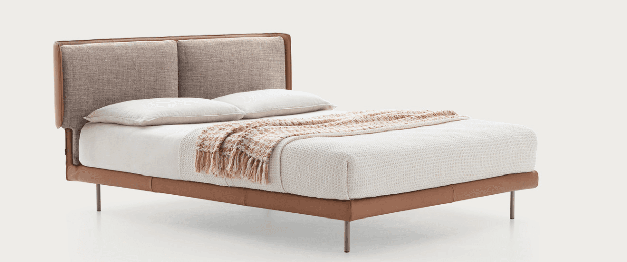 A modern upholstered bed frame with a rectangular headboard featuring two distinct fabric panels. The headboard and frame are accented with smooth tan leather trim. The bed is supported by four thin, cylindrical metal legs. It is dressed with white bedding and a textured throw blanket. — 3D model