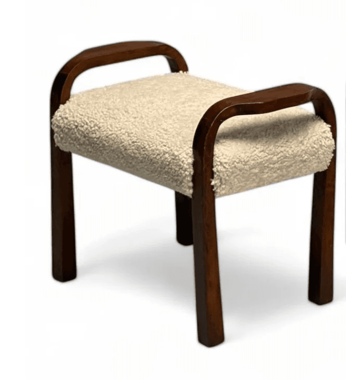 A compact, backless stool featuring a dark brown bentwood frame that gracefully forms both the legs and integrated armrests. The seat is upholstered in a plush, cream-colored sherpa fabric, offering a soft texture contrast to the smooth wood. Its design suggests a blend of functional seating and a decorative accent. — 3D model