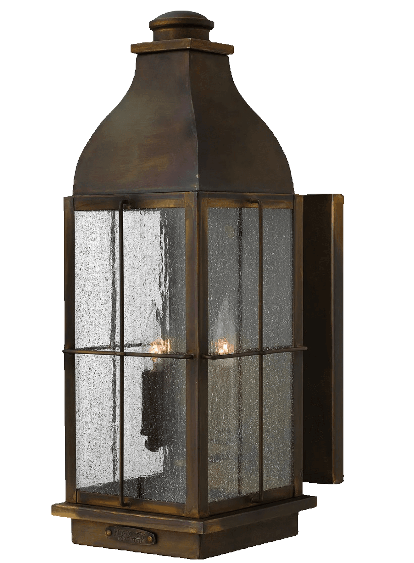 A traditional-style outdoor wall-mounted lantern light fixture. It features a rectangular body with a sloped, peaked roof and a finial at the top. The frame is made of aged bronze-finish metal, enclosing textured, seeded glass panels. Two internal light sources, resembling candelabra bulbs, are visible, casting a warm glow. The fixture has a decorative base designed for secure wall mounting. — 3D model