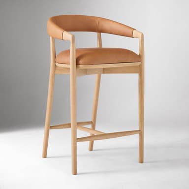 A bar stool with a curved backrest and armrests, featuring a wooden frame and leather upholstery for the seat and back. The frame consists of four cylindrical legs connected by stretchers for stability. The seat is flat and padded, while the backrest is also upholstered and curves to provide lumbar support. The armrests are integrated into the frame structure. — 3D model