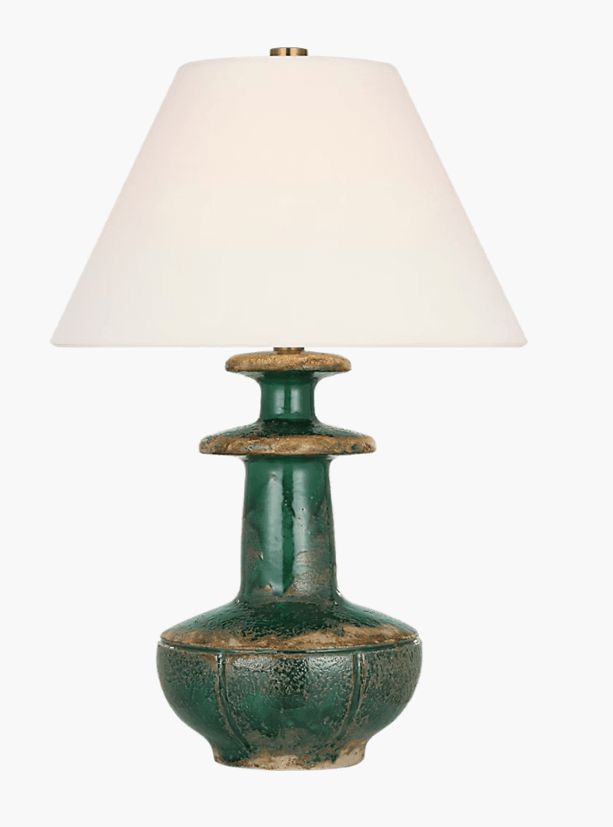 A rustic table lamp featuring a green glazed ceramic base with distressed, earthy-toned accents and a conical fabric shade. The base has a classical urn-like silhouette with a fluted lower body and a tiered neck section. The glaze exhibits a textured, aged appearance, and brass hardware connects the shade to the base. — 3D model