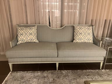 A light grey upholstered sofa featuring an exposed light-toned wooden frame, a gently curved backrest, and tapered legs. The sofa includes two seat cushions and two decorative throw pillows with a geometric pattern. Nailhead trim detailing is present along the base. — 3D model