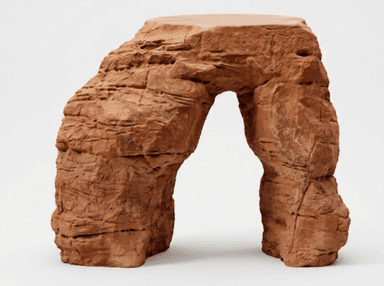 A sculptural accent table designed to resemble a natural rock formation, featuring a distinctive arched structure in a reddish-brown, terracotta hue. The surface is textured to mimic rough, layered stone, with a flat, smooth top suitable for holding objects. — 3D model