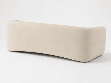 A contemporary upholstered sofa featuring a minimalist design with softly rounded armrests and a unified, clean aesthetic. The sofa is covered in a light beige, textured fabric and has a single, long seat cushion. The base is also upholstered, creating a continuous profile without visible legs, and exhibits a subtle inward curve at the bottom front. — 3D model