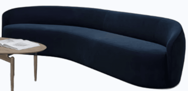 A modern, curved sofa with a deep navy upholstery. The sofa features a continuous, flowing design with a high back and integrated armrests, creating a semi-enclosed seating area. The base is low and seamless with the upholstery. A portion of a round, wooden coffee table with a light wood finish and angled legs is visible to the left, with an open book on its surface. — 3D model