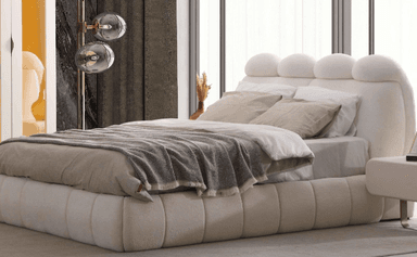 A contemporary low-profile bed featuring a distinctive upholstered headboard and platform base. The headboard is composed of several large, rounded, cloud-like upholstered sections, and the entire bed frame is covered in a textured, light-colored fabric, likely bouclé. It is shown with white bedding, neutral-toned pillows, and a grey throw blanket. — 3D model