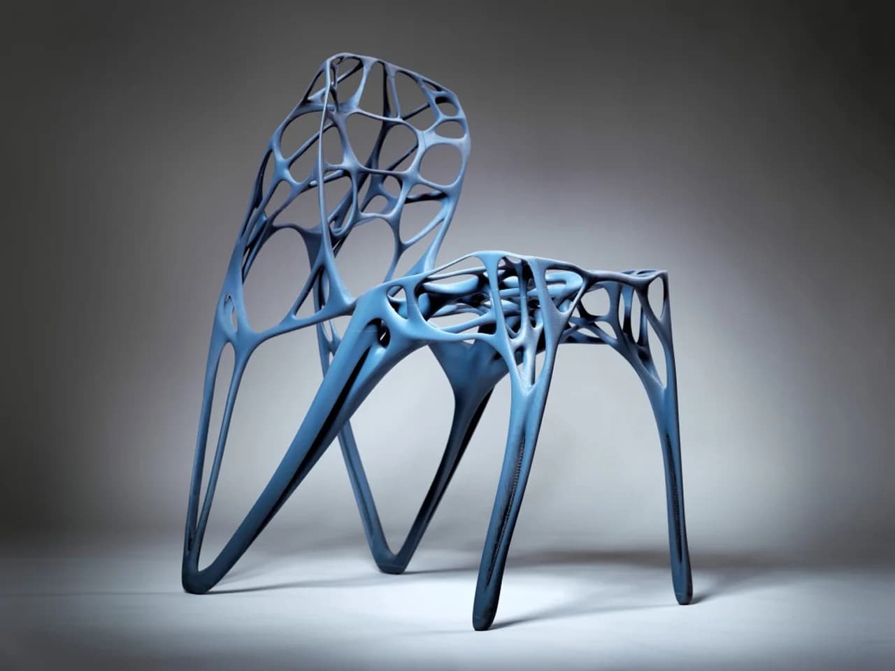 An avant-garde side chair featuring a complex, open cellular structure reminiscent of natural organisms or coral formations. The chair is armless, with its seat, backrest, and legs formed by interconnected, sinuous elements. The design appears to be created through algorithmic or generative design processes, likely 3D-printed from a polymer material. It has a matte, muted blue finish and presents a modern, sculptural aesthetic. — 3D model