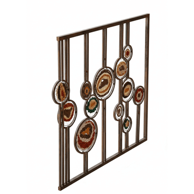 A decorative metal screen serving as a room divider, featuring multiple circular openings filled with varied textile and fiber inlays. The metal frame has a rusted or bronzed finish, and the inserts display intricate woven patterns in natural and earthy tones, including browns, creams, reds, greens, and oranges. The screen is situated outdoors, possibly on a deck or balcony overlooking a body of water and natural landscape. — 3D model