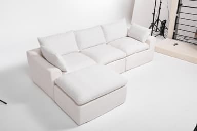 A modular sectional sofa with an attached ottoman. The sofa features deep, plush cushions and a low profile. It is upholstered in a textured white fabric. The configuration shown includes a corner section, two seat cushions, and an ottoman. The design is contemporary and emphasizes comfort. — 3D model