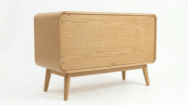 A contemporary, low-profile storage cabinet crafted from light-colored oak wood, featuring smoothly rounded corners on the top, sides, and front panel. It stands on four splayed and tapered legs, presenting a minimalist design with a single large front panel that likely functions as a door for enclosed storage. — 3D model
