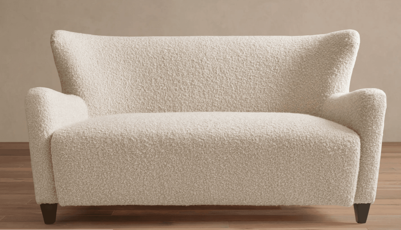 A contemporary two-seater loveseat upholstered in a cream-colored bouclé fabric. It features a high backrest that gently flares outwards at the top, integrated rolled armrests, and a seamless, fully upholstered form. The loveseat is supported by four short, dark, tapered wooden legs. — 3D model