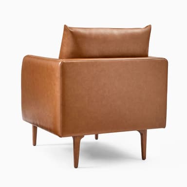 A modern armchair upholstered in brown leather. It features a boxy frame with rounded armrests and a slightly reclined backrest. The seat is composed of two thick cushions. The armchair is supported by four tapered wooden legs, angled outwards. — 3D model