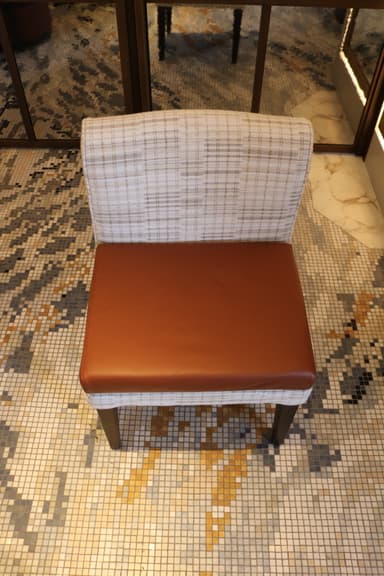 An armless dining chair featuring a light, patterned fabric upholstered back and frame, contrasted with a smooth, warm brown leather seat cushion. The chair stands on four dark, slightly tapered wooden legs. — 3D model