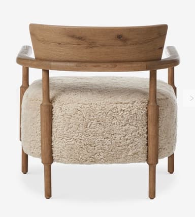 A contemporary armchair featuring a light brown wooden frame and a plush, light beige boucle or sherpa upholstered seat and backrest. The frame includes integrated armrests and subtly shaped legs. The backrest is a curved wooden panel. — 3D model