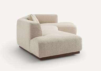 A modular sectional sofa with a low profile and clean lines. The sofa features a textured fabric upholstery and a dark wood base. It is configured with a chaise lounge on the left and a corner section on the right, accompanied by two square throw pillows. — 3D model