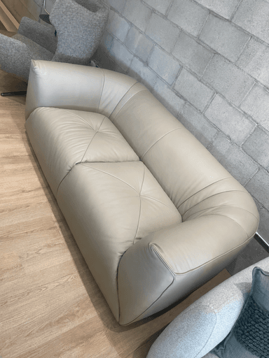A modern two-seater sofa upholstered in light beige leather, featuring a plush, rounded design with a low profile. The backrest shows subtle vertical channeling, and the two individual seat cushions have a gentle tufted appearance. The overall form is volumetric and fluid. — 3D model