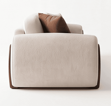 A contemporary upholstered armchair, featuring thick, rounded cushioning in a textured, off-white fabric. The chair incorporates dark wooden side panels that run vertically along its exterior. A loose, rectangular brown accent pillow rests against the back cushion, adding a touch of contrast. The design emphasizes comfort and a minimalist aesthetic. — 3D model