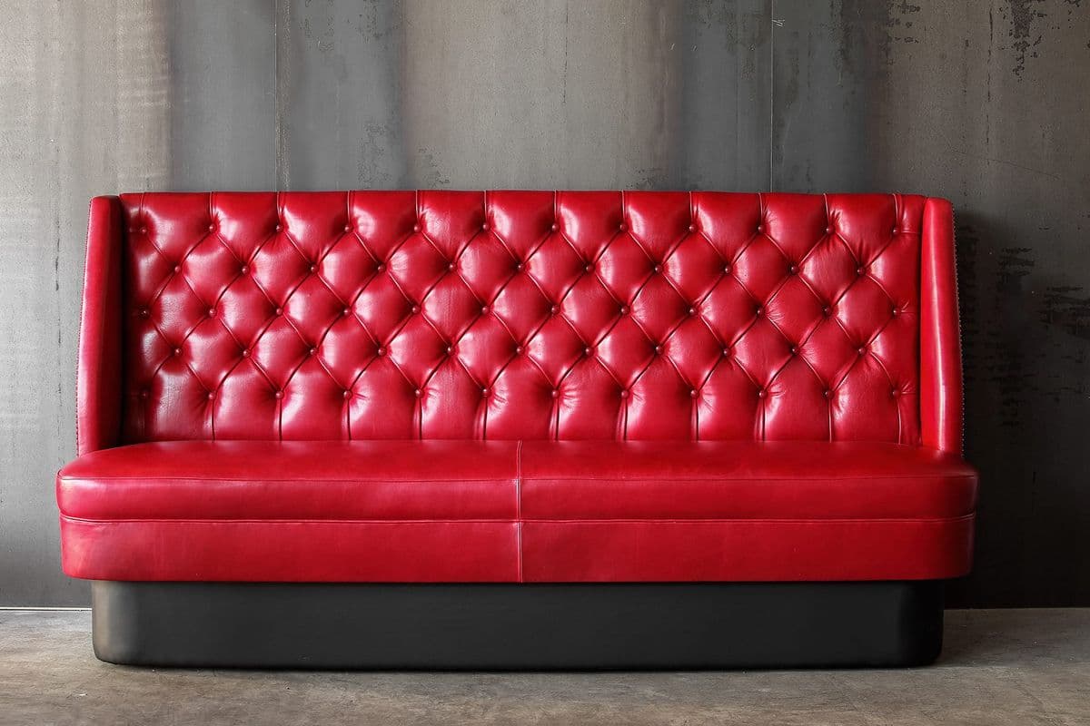 A commercial-grade booth seating unit with a long, straight bench design. It features vibrant red upholstery on both the seat and the deeply button-tufted backrest, set upon a recessed black plinth base. — 3D model