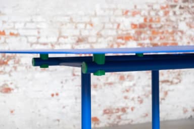 A long, modular dining table featuring three distinct segments with rounded ends, supported by a vibrant blue tubular metal frame. Each segment's top is dark blue, complementing the bright blue base, with small green connectors and feet accents. — 3D model
