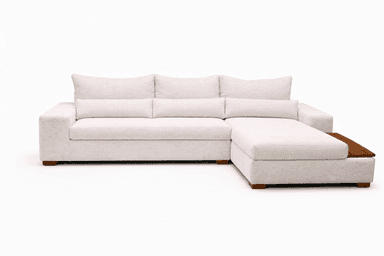 An L-shaped sectional sofa upholstered in a light beige, textured fabric. The sofa consists of three main seat cushions and a left-hand facing chaise. It features plush, loose back cushions and two cylindrical bolster pillows. The base is low-profile with short, square wooden block feet. — 3D model