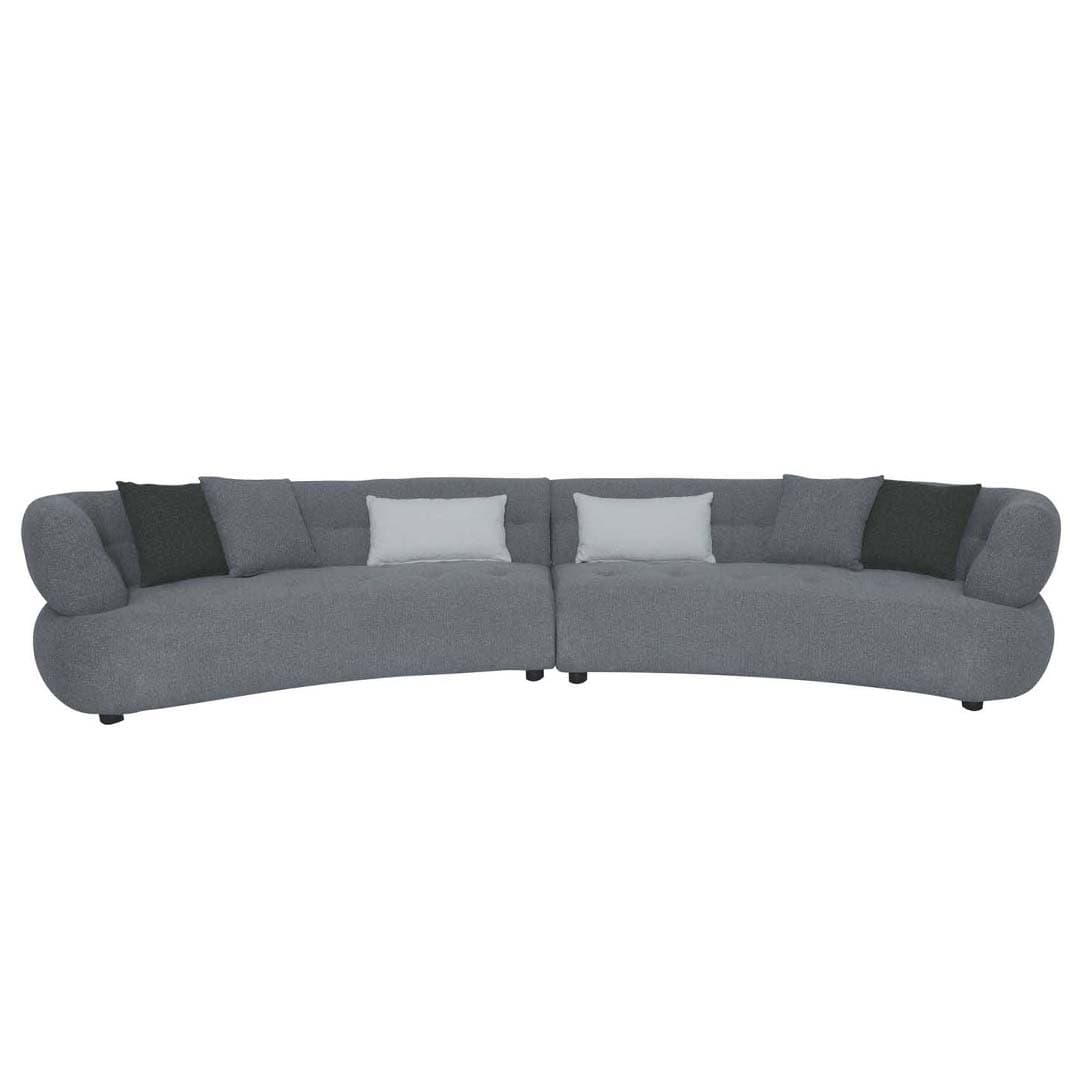 A contemporary curved modular sectional sofa upholstered in a textured grey fabric. The sofa comprises two distinct sections joined to form a sweeping curve, featuring rounded, soft forms and integrated armrests that flow seamlessly from the backrest. It is styled with several accent pillows in contrasting dark grey and light grey/off-white tones. The design suggests a comfortable and inviting seating arrangement for a modern living space. — 3D model