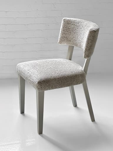 An armless dining chair featuring a light-colored, textured upholstered seat and a distinctively curved, wraparound backrest. The chair is supported by four straight, tapered legs, finished in a light grey or off-white color, matching the general light aesthetic of the piece. — 3D model