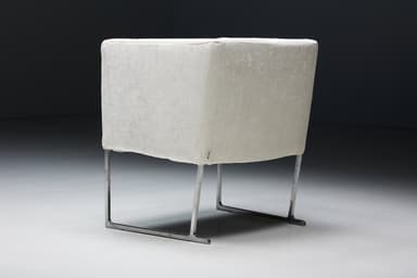 A set of four identical armchairs with a modern design. Each armchair features a cube-like upholstered seat and backrest with squared arms. The upholstery appears to be a textured fabric. The chairs are supported by a sleek, minimalist frame, likely made of polished metal, elevating them slightly off the ground. The overall aesthetic suggests a contemporary or minimalist style. — 3D model