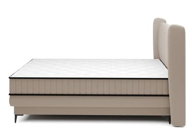 A contemporary upholstered bed featuring a distinctive wingback headboard and an integrated box spring base. The entire structure, including the headboard and base, is covered in a soft beige fabric with vertical channel tufting on the headboard and upper box spring. The bed is supported by subtle, tapered black metal feet. A white mattress with black piping is positioned on top of the box spring. — 3D model