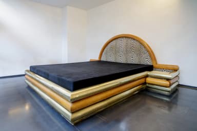 A bed frame with a distinctive design, featuring layered cylindrical elements in wood and brass around the base, and a semicircular headboard upholstered in a leopard-print fabric, framed by polished wood. — 3D model