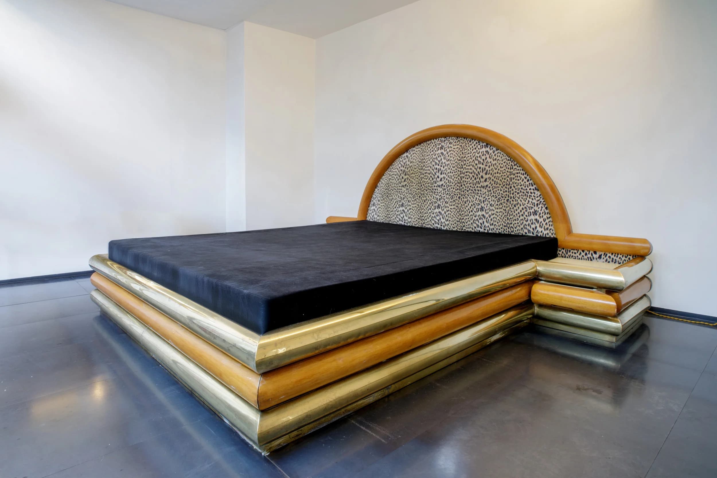 A bed frame with a distinctive design, featuring layered cylindrical elements in wood and brass around the base, and a semicircular headboard upholstered in a leopard-print fabric, framed by polished wood. — 3D model