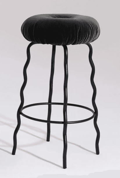 A modern bar stool featuring a deeply cushioned, round seat upholstered in dark grey velvet, distinguished by a central button tuft. The stool's black metal frame consists of four legs, each uniquely designed with a continuous wavy or squiggly profile, extending from beneath the seat to the floor. A circular black metal footrest connects the legs approximately one-third of the way up from the base, providing stability and support. The overall design conveys a playful yet sophisticated contemporary aesthetic. — 3D model