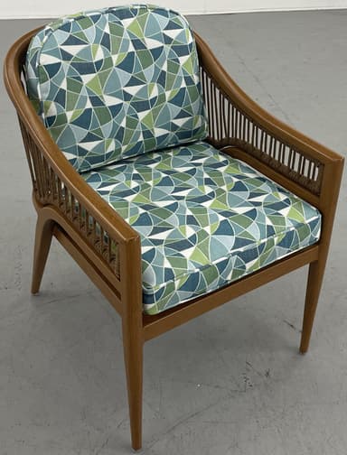 A barrel-back armchair featuring a warm-toned wooden frame, likely teak or oak, with distinctive woven or rope detailing along the arms and backrest. The chair is upholstered with removable seat and back cushions in a textured, multi-tonal green, white, and blue striped fabric. Its design combines elegant curves with a relaxed, tropical-modern aesthetic. — 3D model