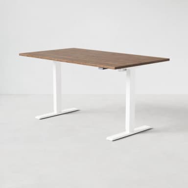 A modern standing desk with a rectangular, wood-grain finished top and white, adjustable legs. The legs have a curved, minimalist design with a flat base for stability. A visible mechanism on the right leg suggests height adjustability. — 3D model