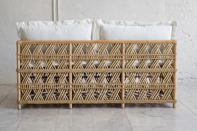 A rattan daybed with a woven geometric pattern on the sides and back. It features thin, cylindrical legs and is topped with two white pillows and a white mattress or cushion. — 3D model