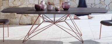 A rectangular coffee table with rounded corners, featuring a dark brown top and a delicate, wireframe base composed of thin, angled metal rods in a copper finish. The base has a distinct, starburst or Eiffel Tower-inspired design. — 3D model